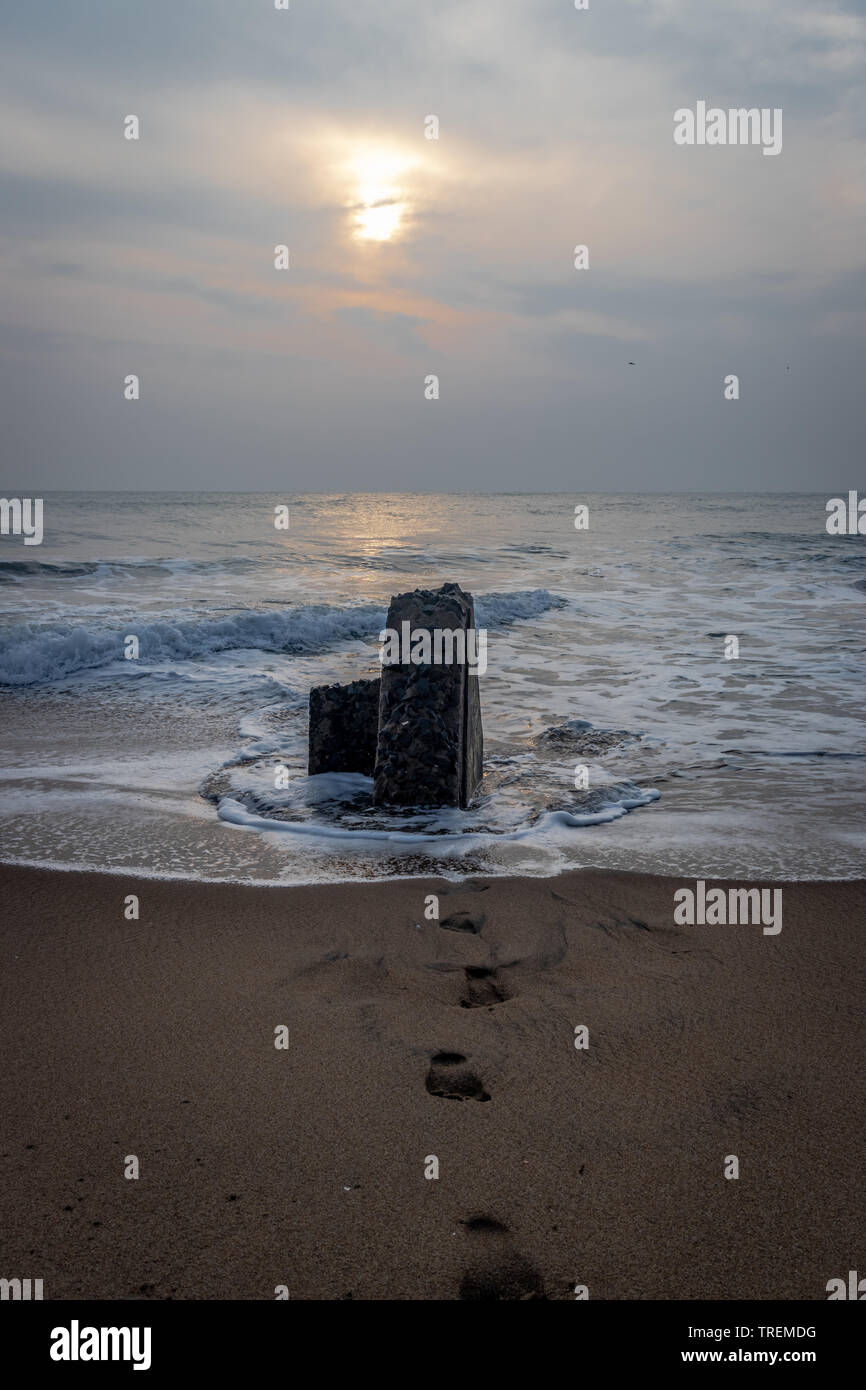 Sunrise over rock and footprints of nature lover in sandy beach of pondicheery india. Stock Photo