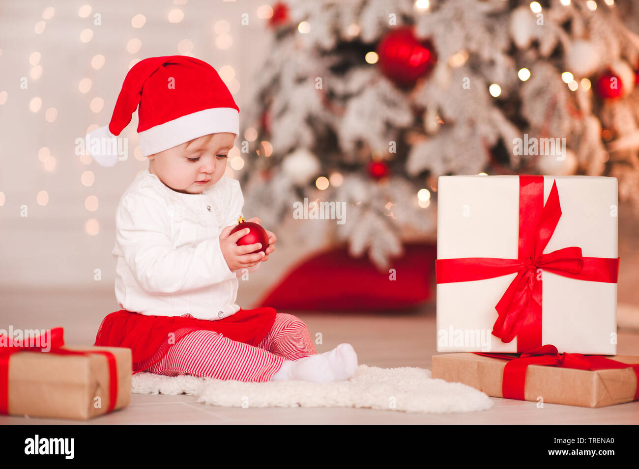 Cute baby girl 1 year old wearing santa hat posing over Christmas  background. Sitting on floor with Christmas ball. Holiday season Stock  Photo - Alamy