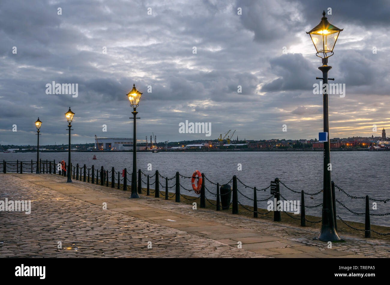 Deserted riverside cobblestone path lined with stret lights in Liverpool  and cloudy sky at dusk Stock Photo