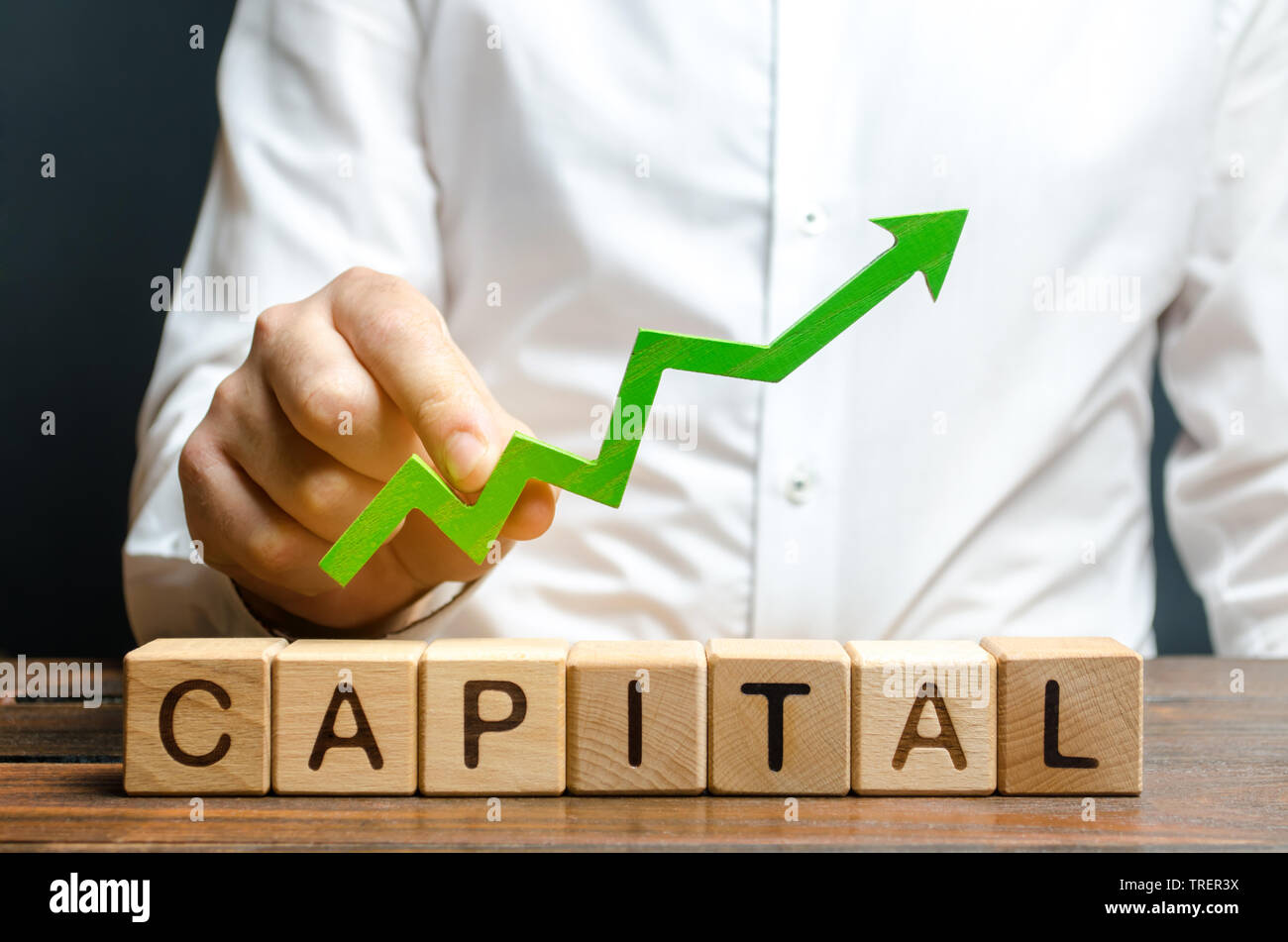 A businessman is holding a green up arrow above the word Capital. Increasing the attractiveness of the conditions for business, increasing the flow of Stock Photo
