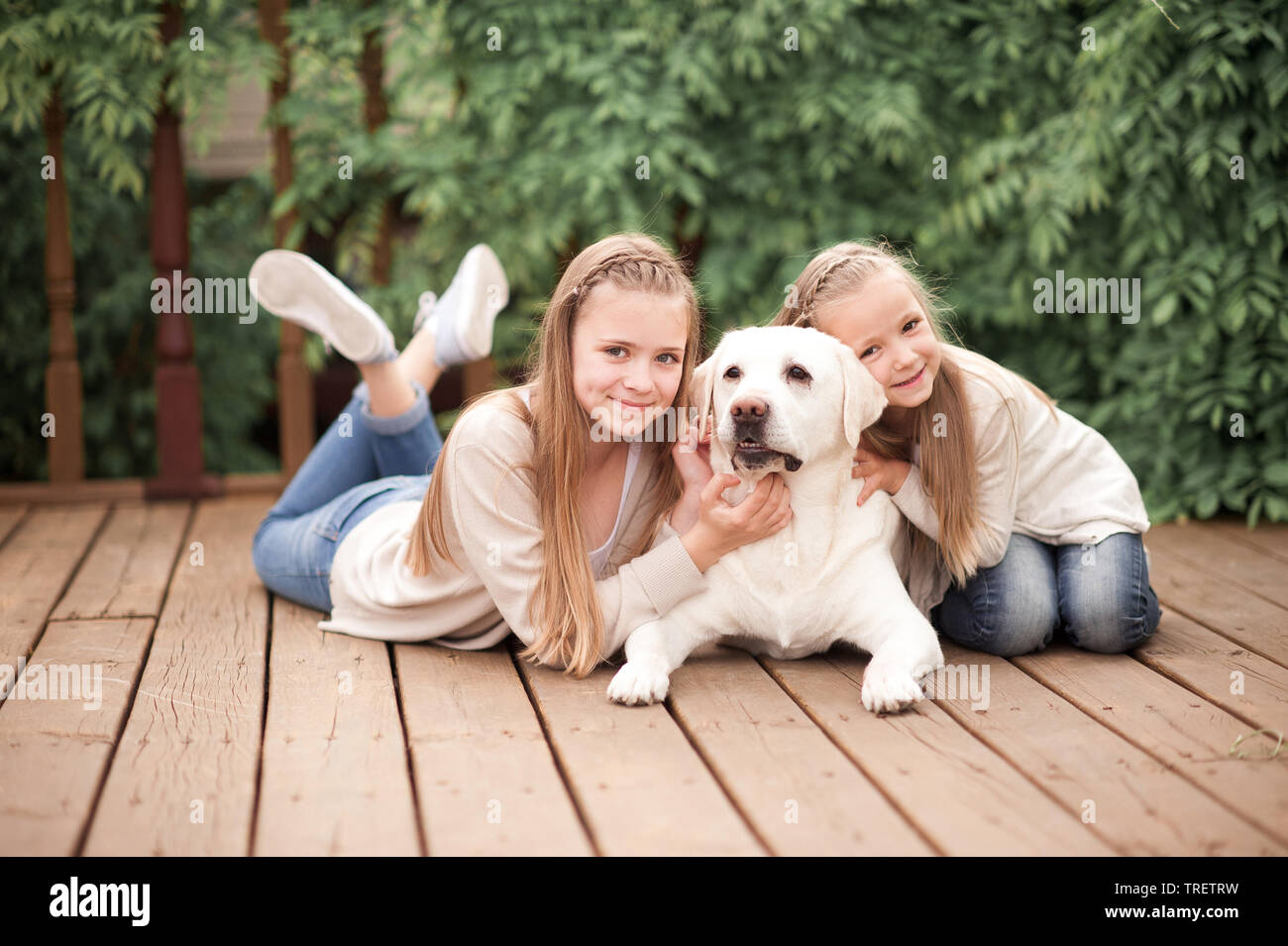 Happy girls having fun with pet labrador outdoors. Lying on wooden floor. Looking at camera. Happiness. Togetherness. Stock Photo