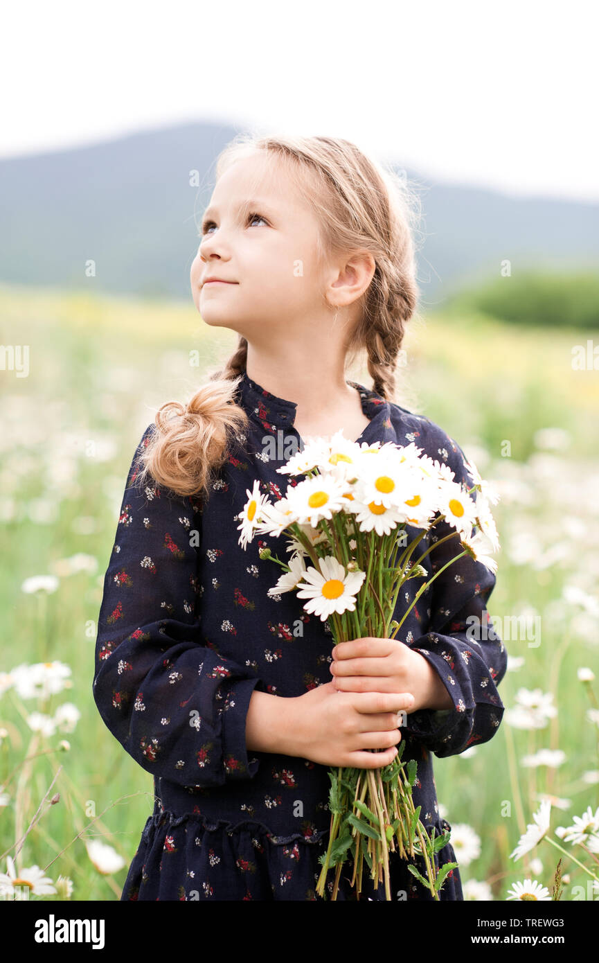 Cute kid girl 4-5 year old holding flowers outdoors. Looking away. Summer season. Stock Photo