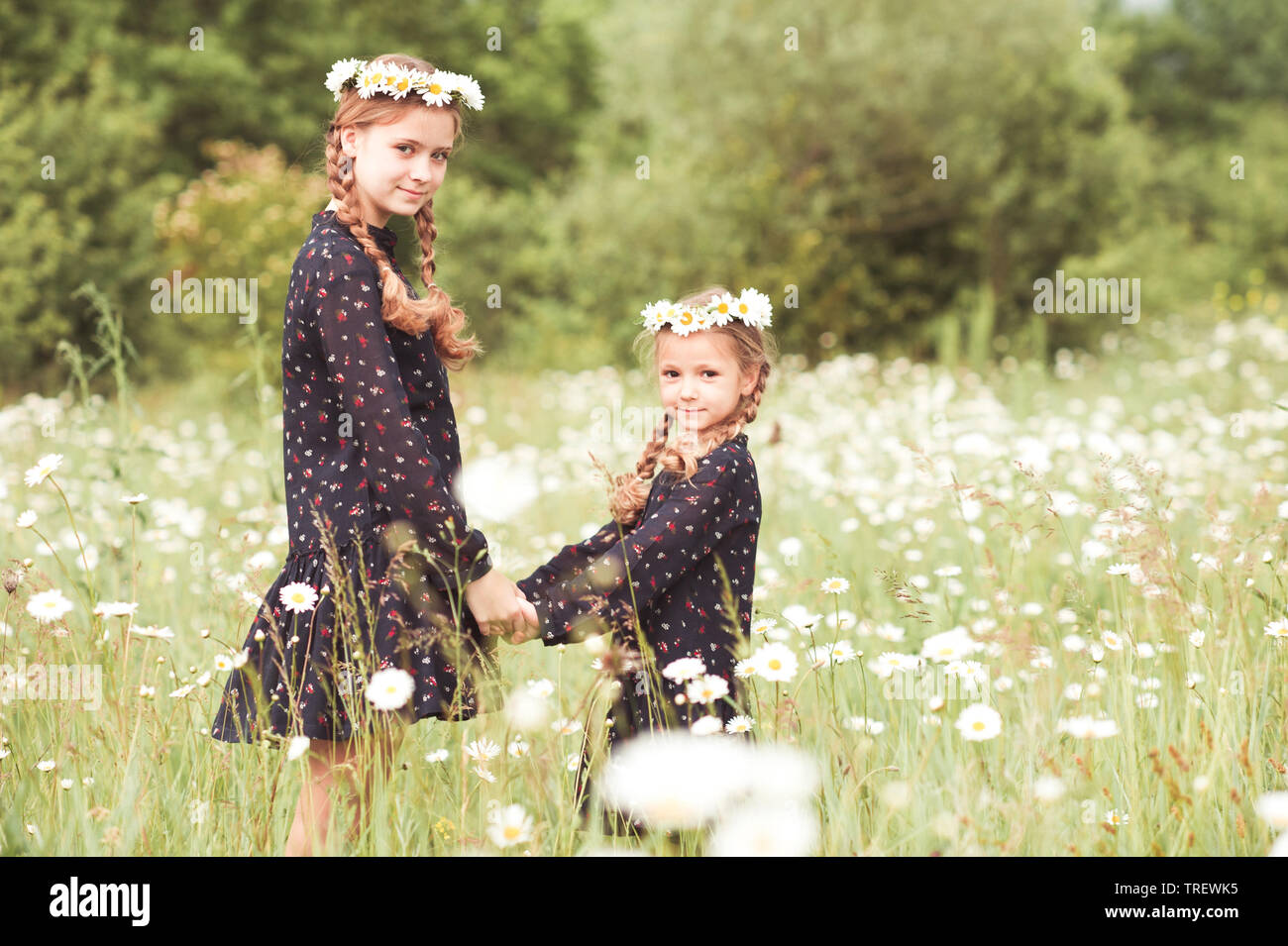 Smiling girls standing in chamomile meadow. Posing outdoors. Looking at camera. Childhood. Stock Photo