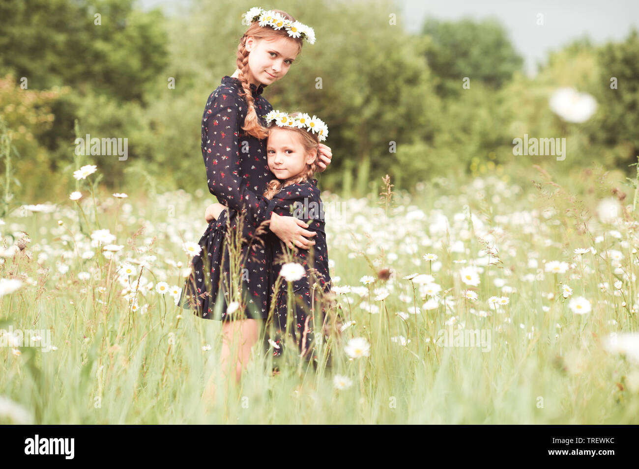 Smiling girls standing in chamomile meadow. Posing outdoors. Looking at camera. Childhood. Stock Photo