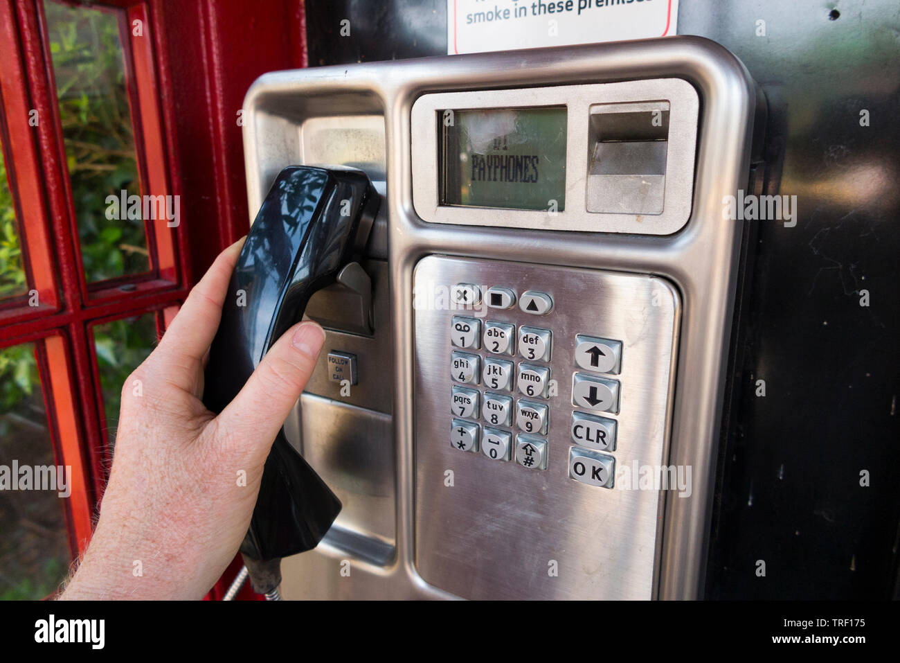 Person lifting the handset and preparing to dial a number / dialling from a late model coin operated public telephone / payphone pay phone in an original red / call box. England UK Stock Photo