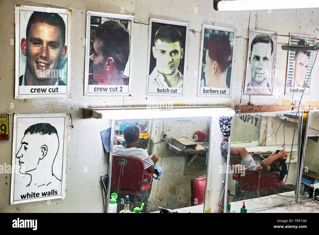 Puerto Princesa City, Palawan, Philippines: Pictures of sample hair cuts and mirrors hanging at a wall in an old barber shop Stock Photo