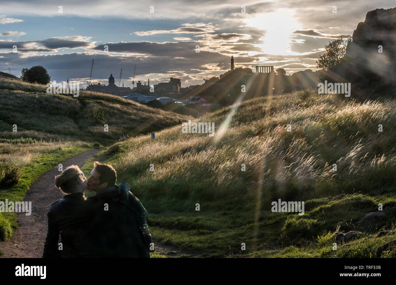 Lovers enjoying the dramatic light across Holyrood Park looking Calton Hill Stock Photo