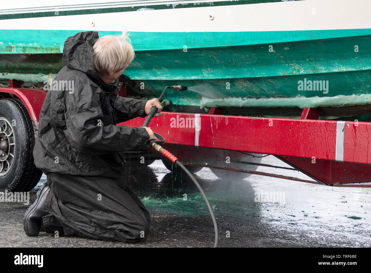Caucasian man cleaning boat hull with pressure washer Stock Photo