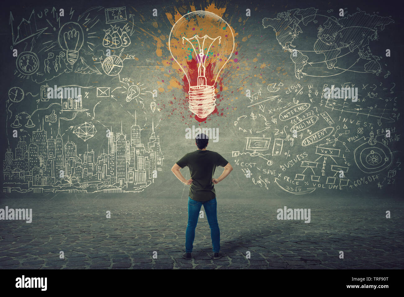 Rear view of confident young man, hands on hips, stands in front of a wall with drawn colorful light bulb and business sketches. Uniqueness of the ide Stock Photo