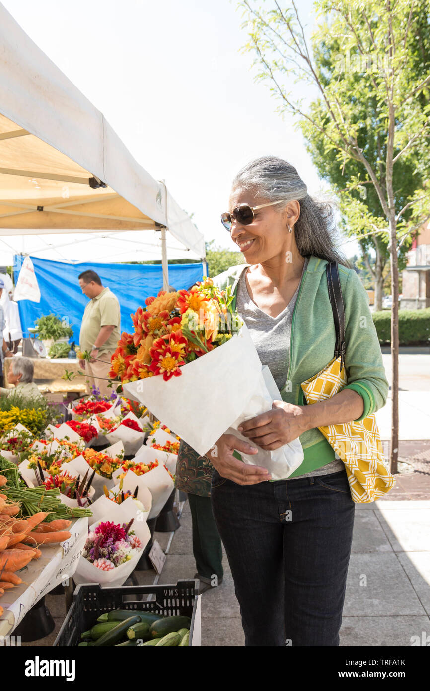 Happy, middle-aged black African American woman shopping for flowers at farmer's market. Healthy mature lifestyles. Stock Photo