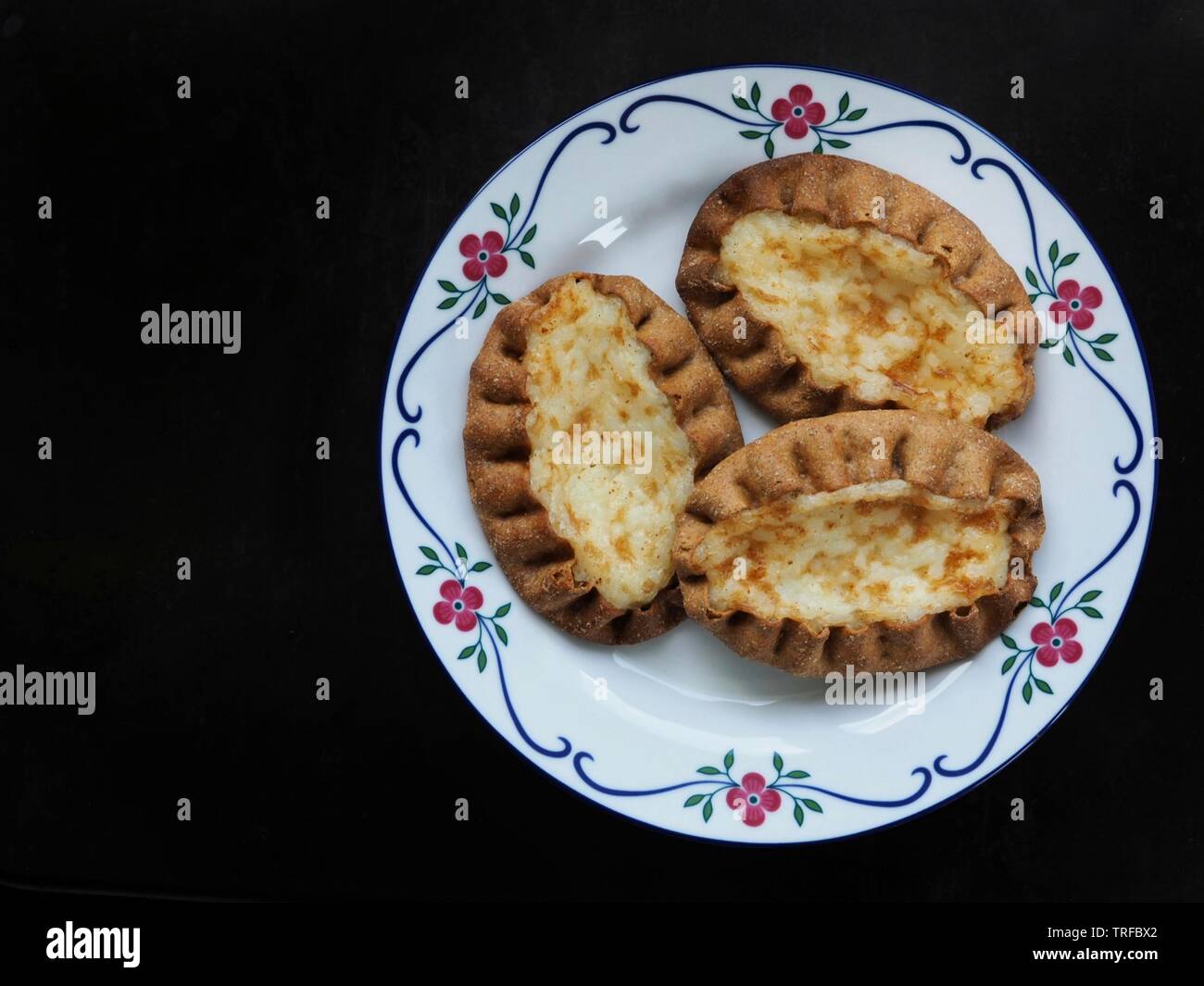 Traditional Finnish cuisine. Karelian pies on a plate on black background with copy space. Stock Photo