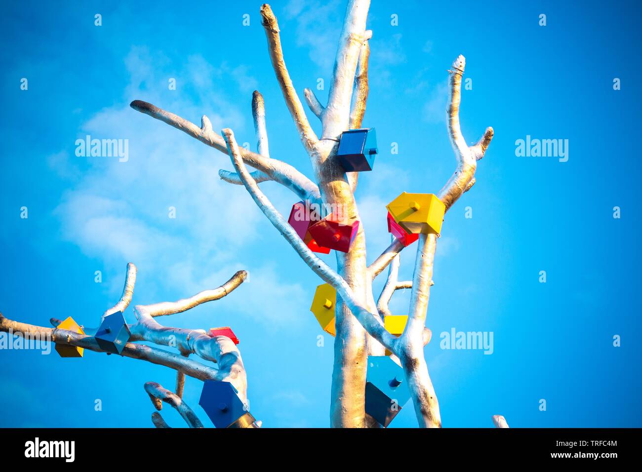 Feeders for birds are attached to a tree made of metal. The tree is against the blue and clear sky Stock Photo