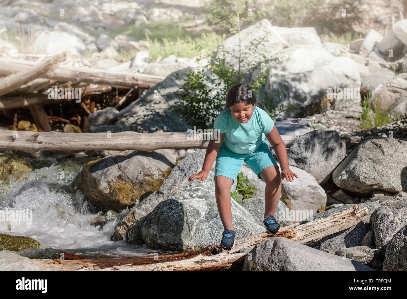 A little girl crossing a wooden log over river rapids during summer camp, weight loss activity for children. Stock Photo