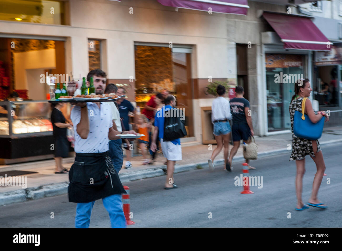 A waiter rushes to his client across the street, Nea Peramos, Greece Stock Photo