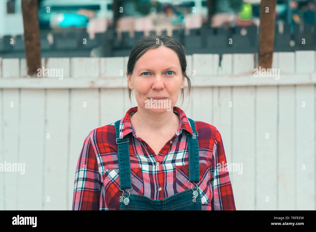 Serious female farmer posing on farm. Confident woman farm worker wearing plaid shirt and jeans overalls looking at camera. Stock Photo