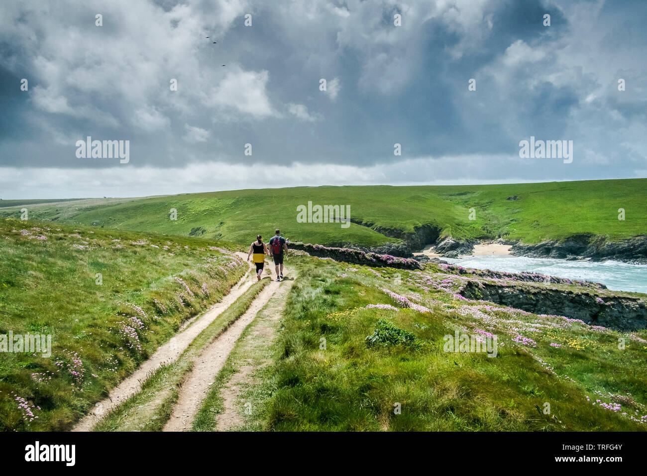 People walking along the South West Coast Path on wild rugged coast at Polly Porth Joke in Newquay in Cornwall. Stock Photo