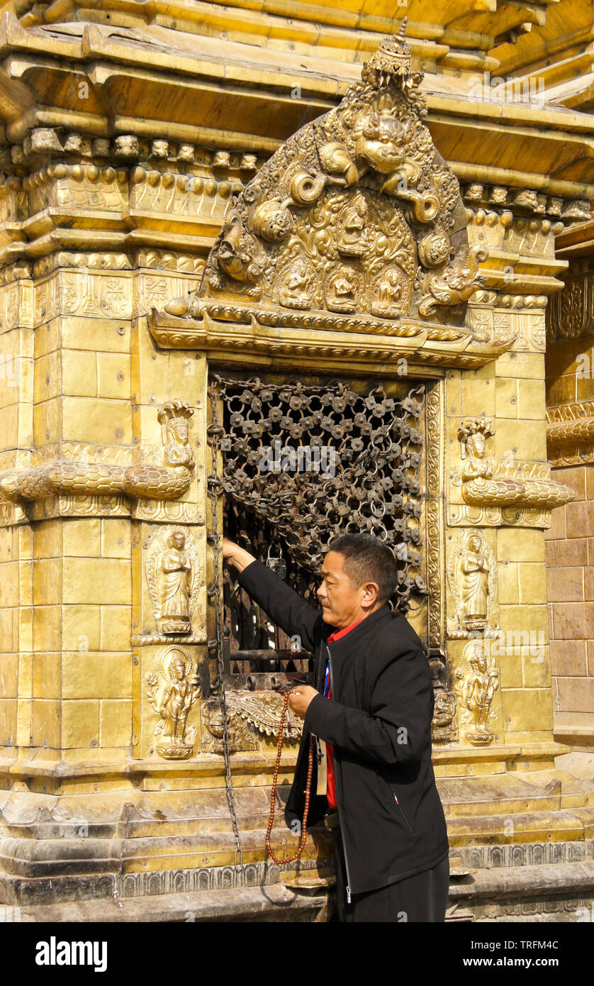Tibetan man with prayer beads worships at a niche (containing a Buddha ...