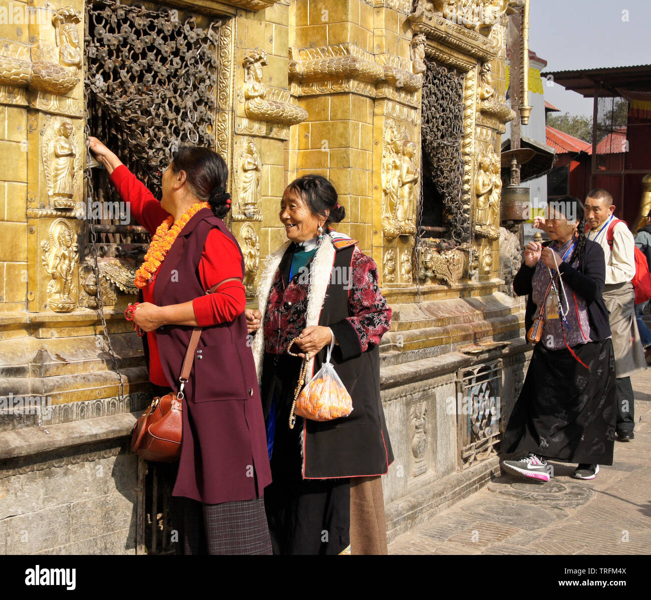 Tibetan pilgrims in traditional dress worshipping at gilded niches of the large stupa at Swayambhunath Buddhist temple, Kathmandu, Kathmandu Valley, N Stock Photo