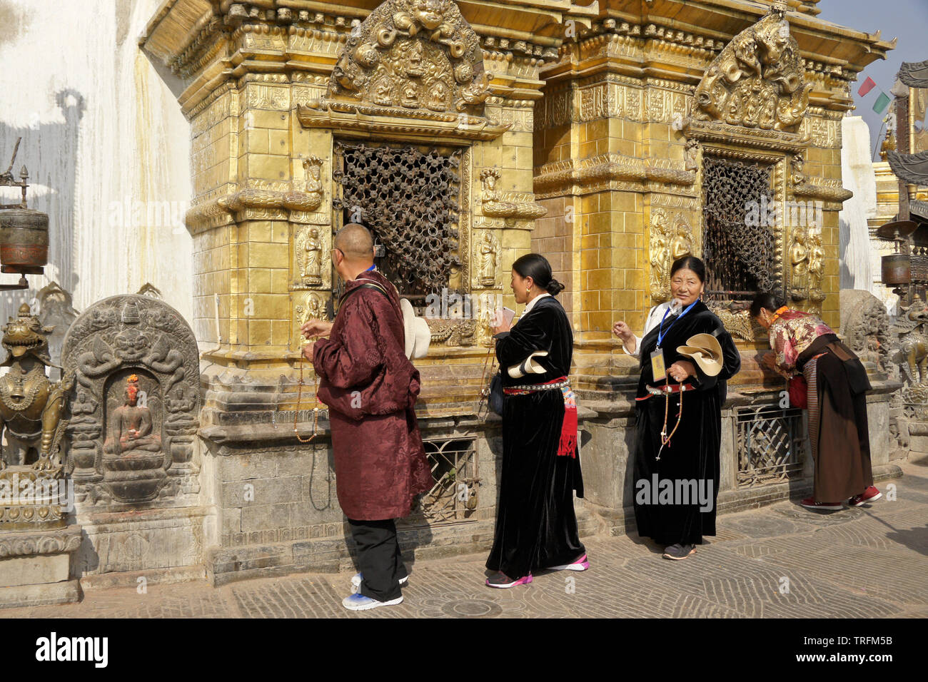 Tibetan pilgrims in traditional dress worshipping at gilded niches of the large stupa at Swayambhunath Buddhist temple, Kathmandu, Kathmandu Valley, N Stock Photo