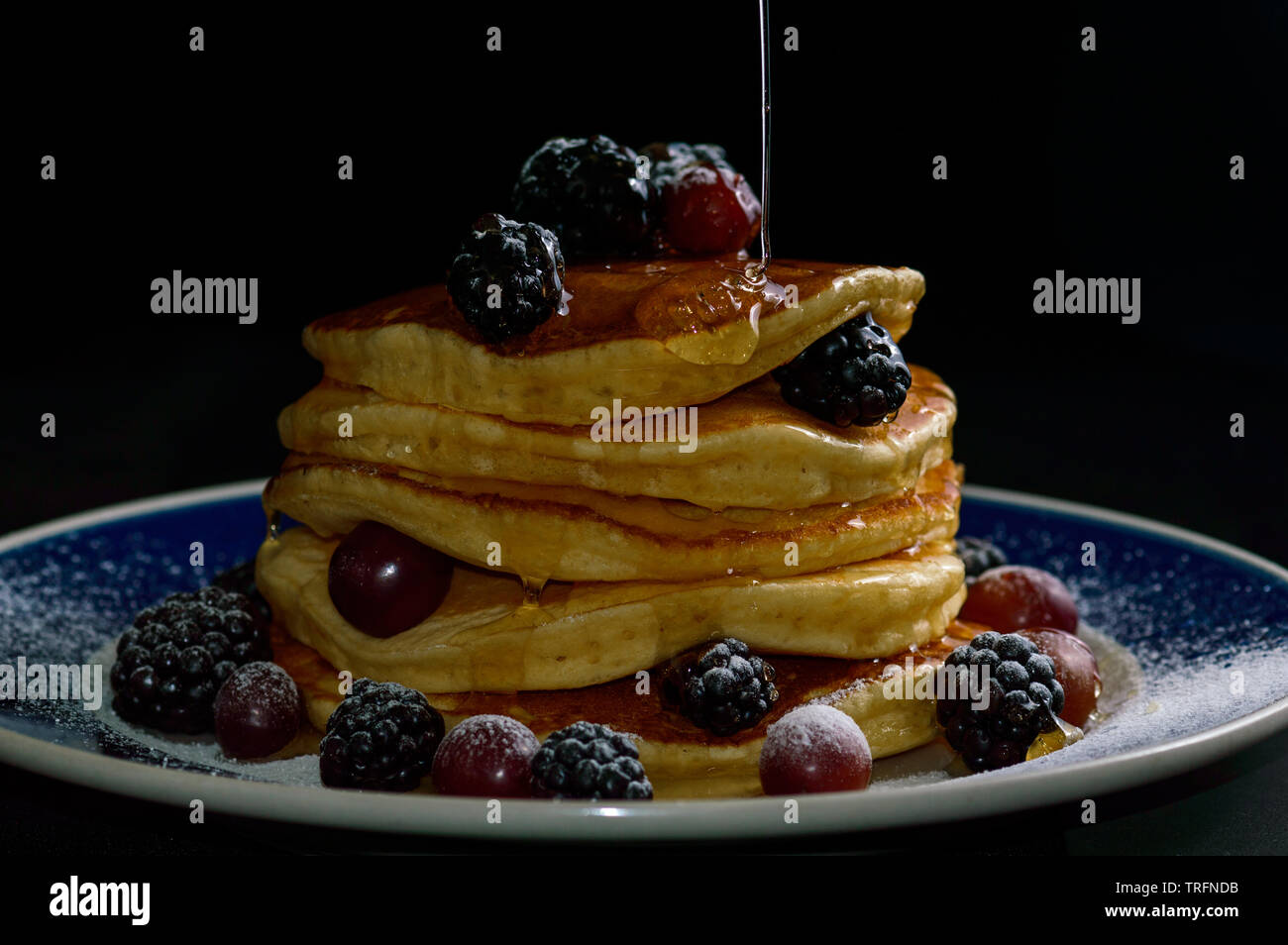 Stacked pancakes with summer berries and dripping honey maple syrup, isolated on black. Food, breakfast,snack. Copy space Stock Photo