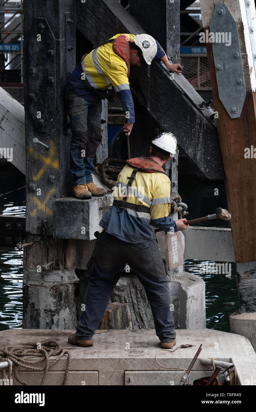 Two man in a hard hats, wield a sledgehammer, repairing the underside of Pyrmont Bridge, Sydney, Australia. Stock Photo