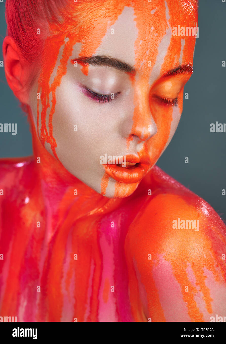 Woman model with makeup and leaking orange neon paint. Glitter vivid makeup. High fashion model Stock Photo