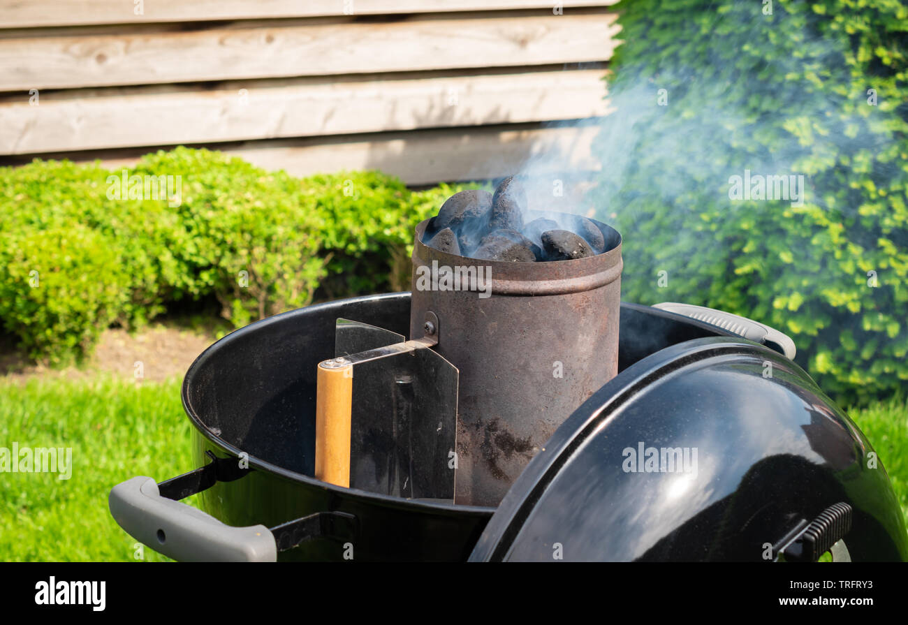 Smoking charcoal briquettes in a chimney starter prepared for a garden barbecue party. Stock Photo