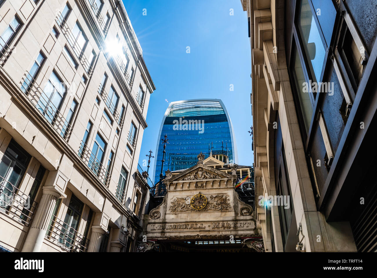 London, UK - May 14, 2019:  Low angle view of the entrance to Leadenhall Market and The Gherkin skyscraper in the City of London against blue sky. Stock Photo