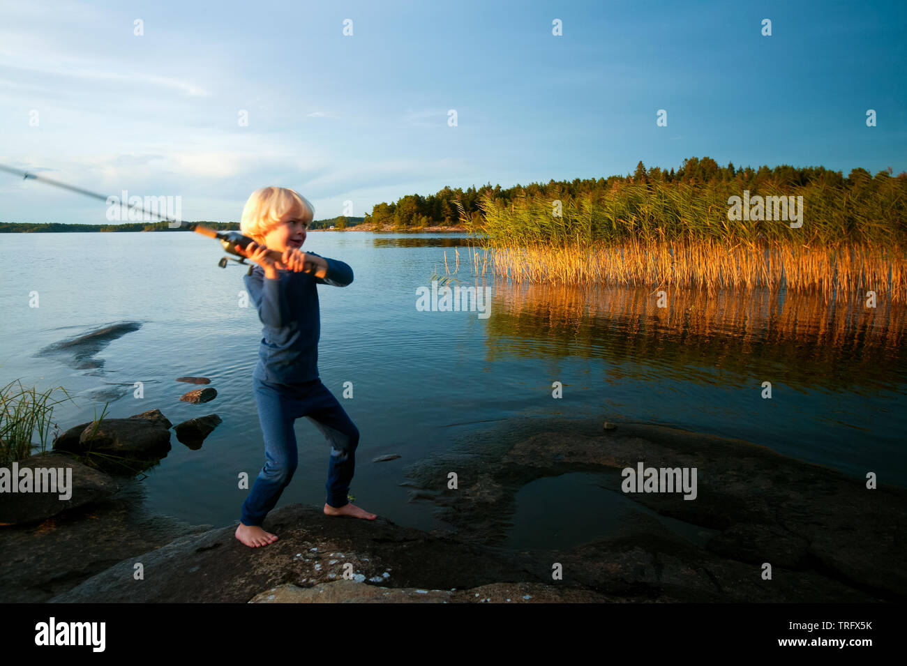 A young boy is fishing at the island Brattholmen in the lake Vansjø, Østfold, Norway. Vansjø is the largest lake in Østfold. The lake Vansjø and its surrounding lakes and rivers are a part of the water system called Morsavassdraget. September, 2006. Stock Photo