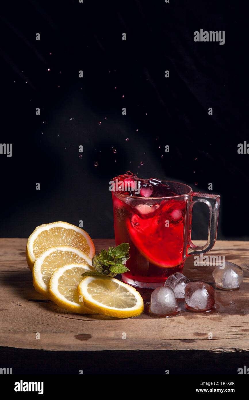 Summer iced drink - hibiscus cold tea with ice, lemon and mint.  Big splash with drops of hibiscus cold tea from the glass of beverage with fallen lem Stock Photo