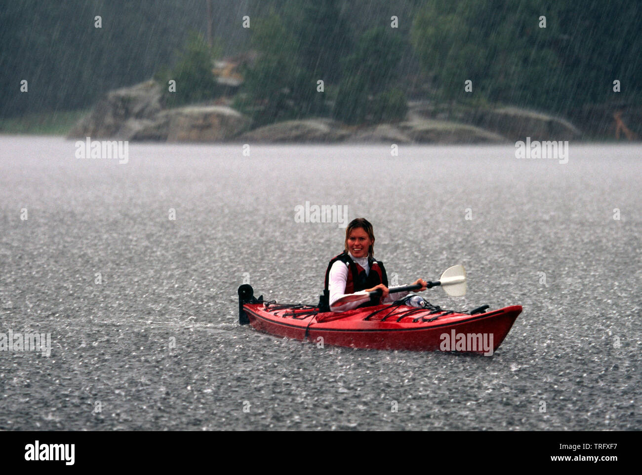 Female paddler in a kayak during a heavy rainfall on the lake Vansjø in Østfold, Norway. The lake Vansjø and its surrounding lakes and rivers are a part of the water system called Morsavassdraget. June, 2004. Stock Photo