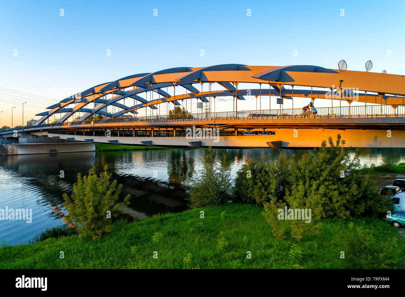 Suspension bridge Kotlarski  over the Vistula River in Krakow, Poland, in sunset light with unrecognizable cyclists. Stock Photo