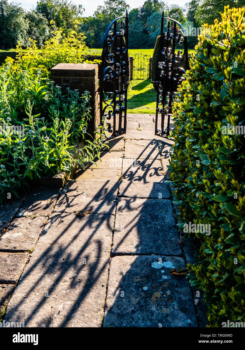 Shadows on a stone path leading to a gate into an English country garden in Derbyshire UK Stock Photo