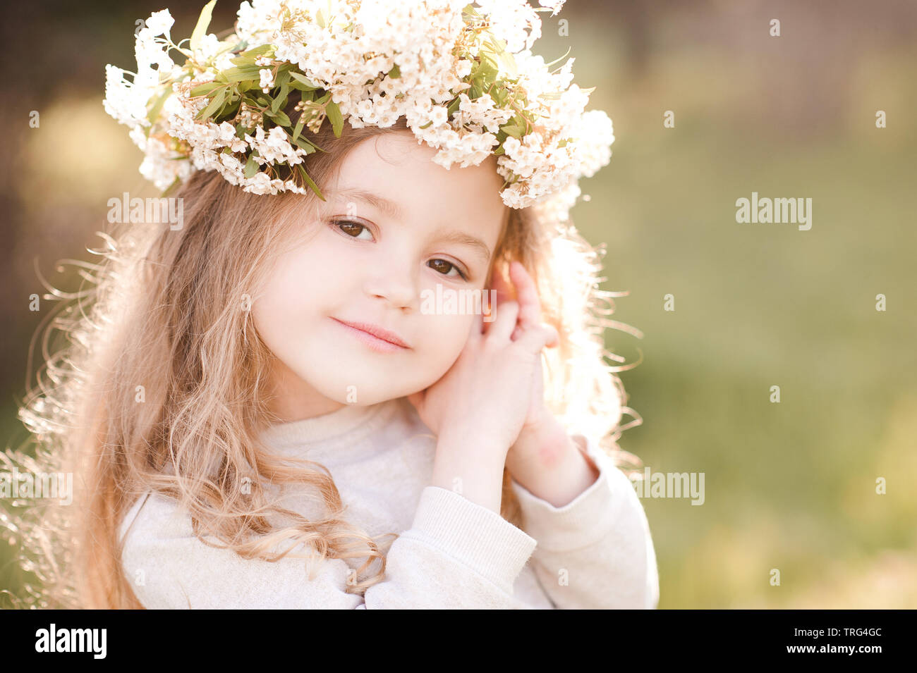 Cute baby girl 3-4 year old wearing floral wreath outdoors. Looking at camera. Spring season. Stock Photo