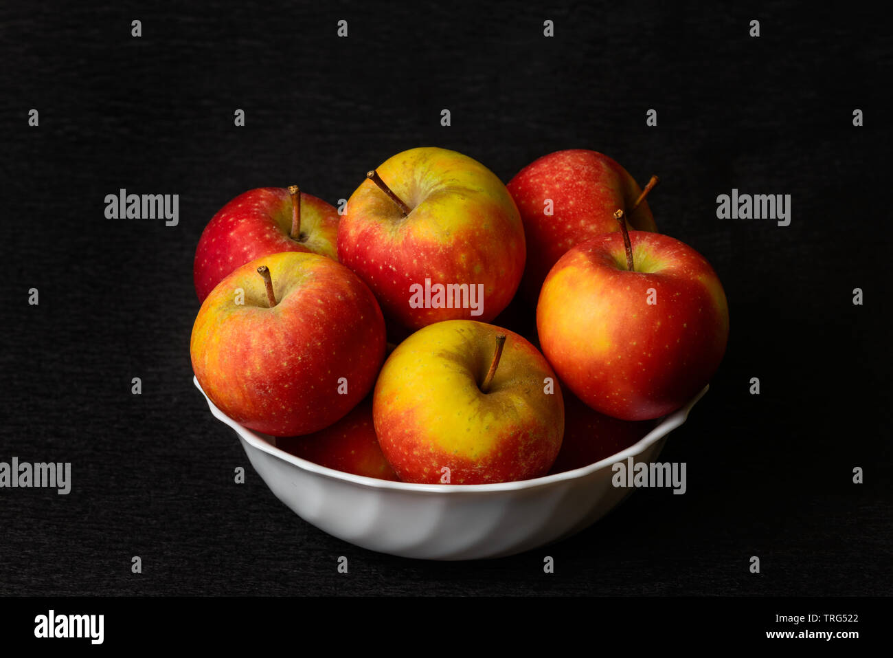 Piles of apples. Still life red apples. Nature morte of red apples in white bowl on black background. Stock Photo