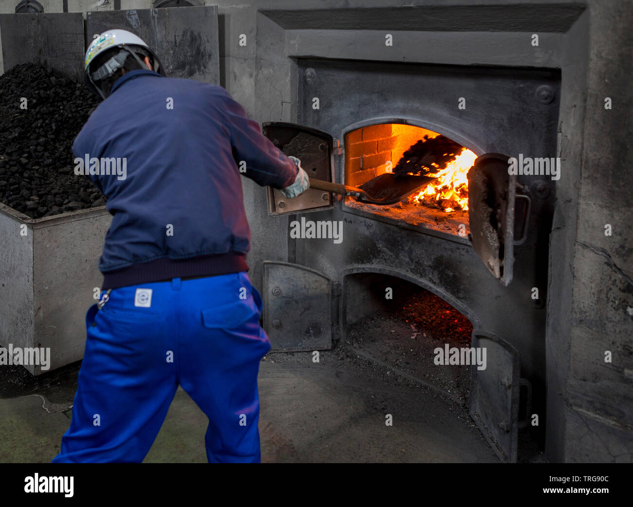Man stoking fire under a pot still at a Japanese whisky distillery, Hokkaido, Japan. Stock Photo