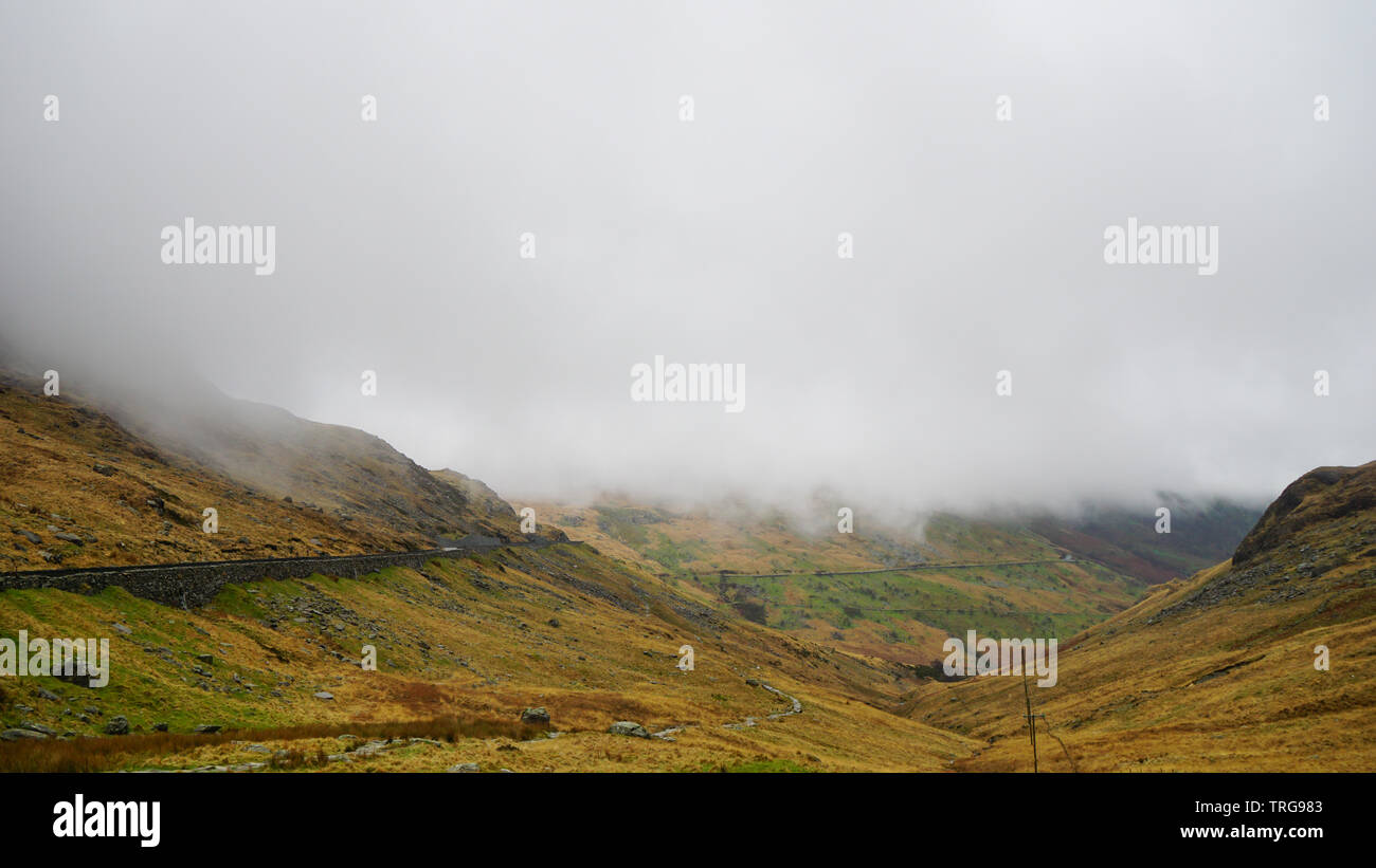 Stunning landscape with foggy and moody skies among the mountains, covered with beautiful snow – captured during a hike at Snowdon in winter (Snowdoni Stock Photo