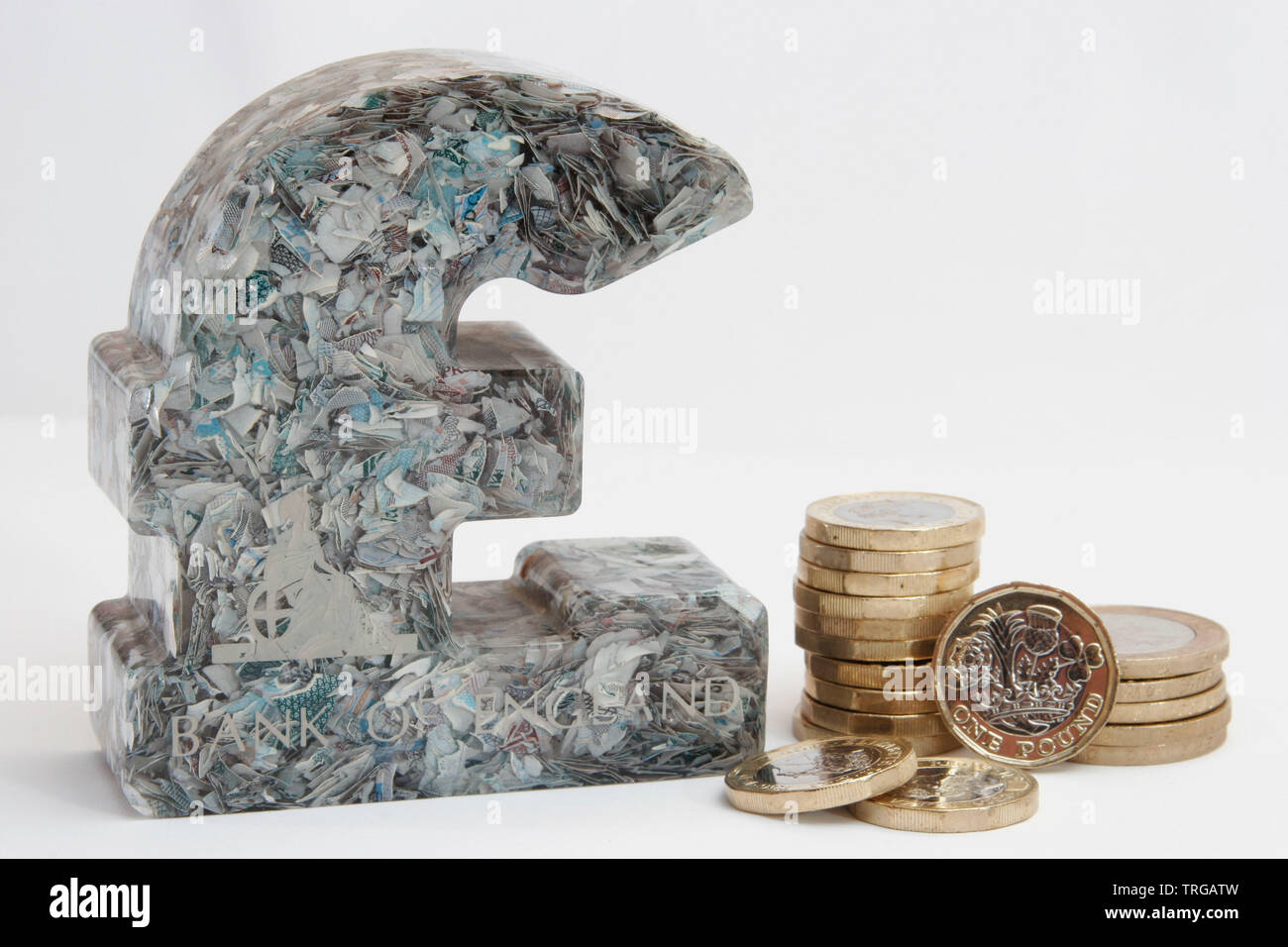 British Pound paper weight made from chopped up £5 notes next to £1 coins and notes UK Stock Photo