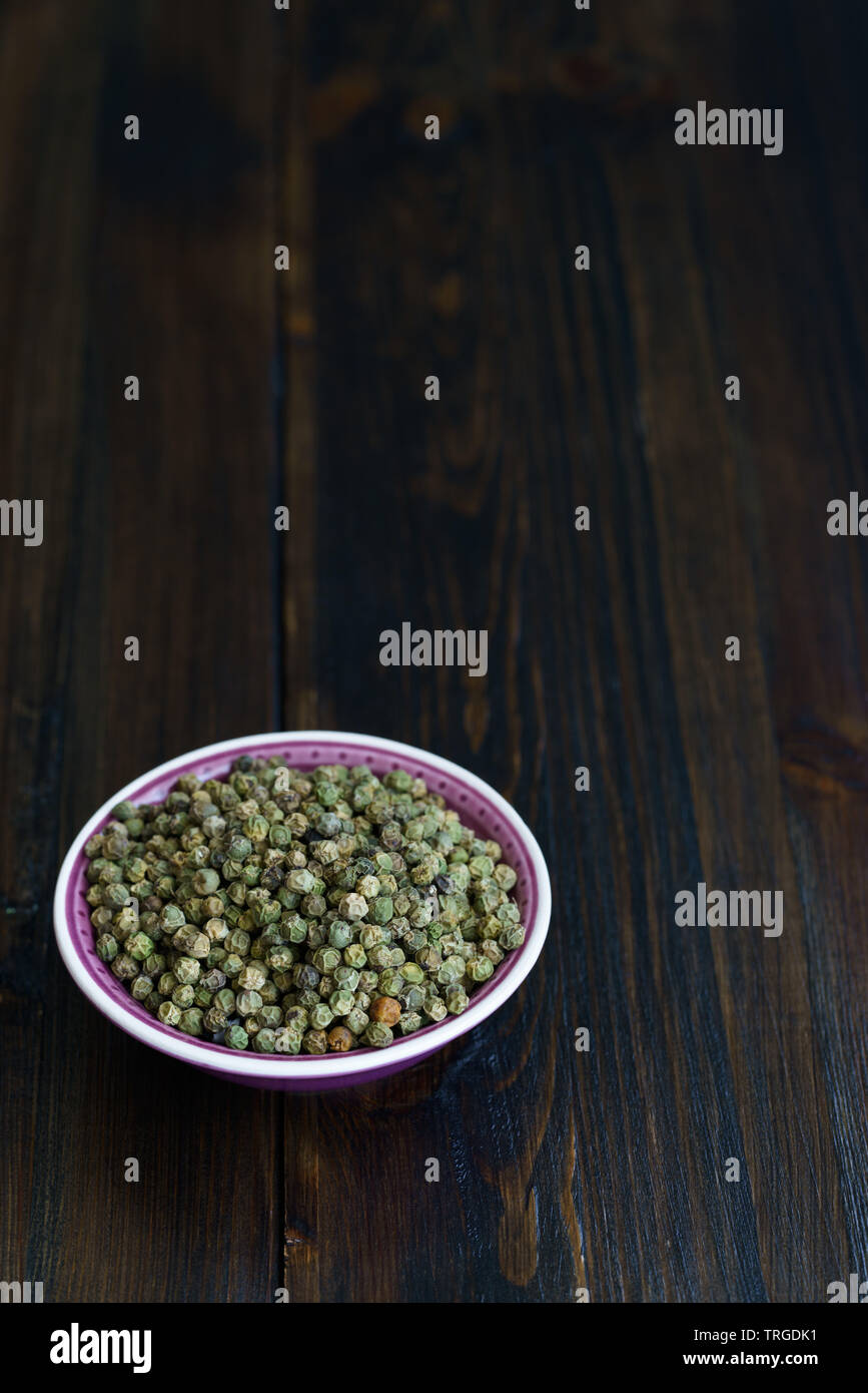 Dried green peppercorns in a violet bowl. Dark wooden table, high
