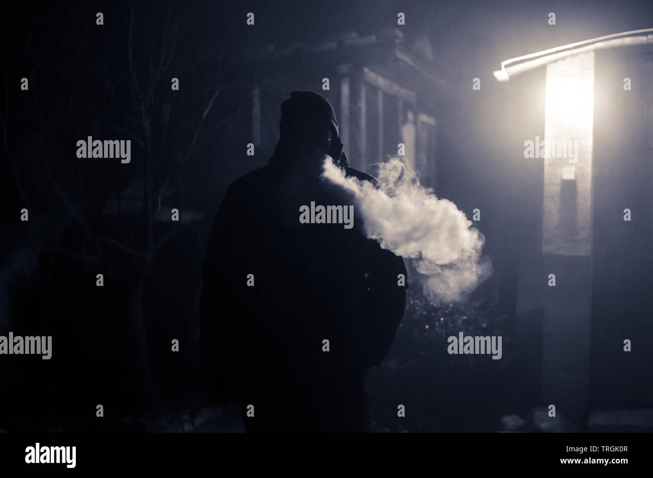 adult man smoking at night making a big smoke effect in back light Stock Photo