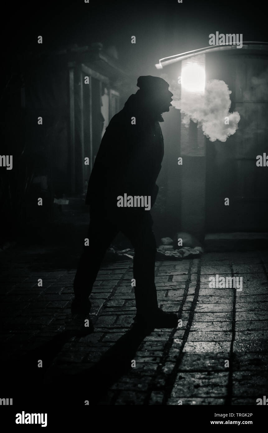 man silhouette smoking like chimney at night with backlight Stock Photo