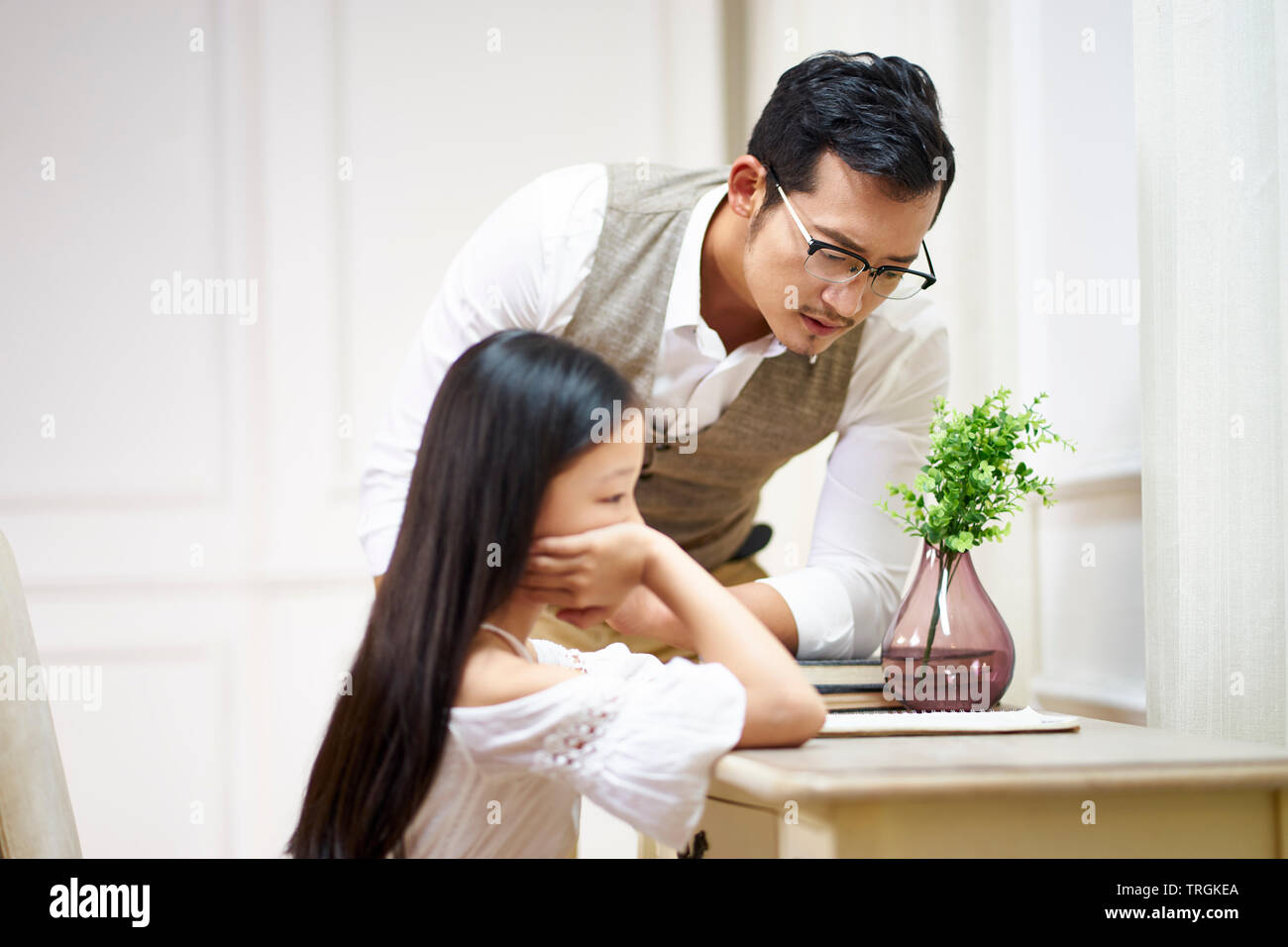 young asian father looking at what's written or drawn by his unhappy daughter. Stock Photo