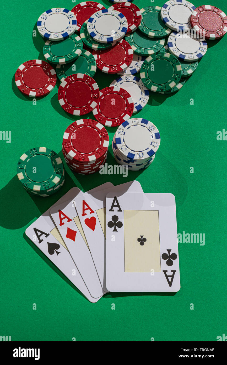 Four aces and poker chips, on green surface, with afternoon sunlight Stock Photo