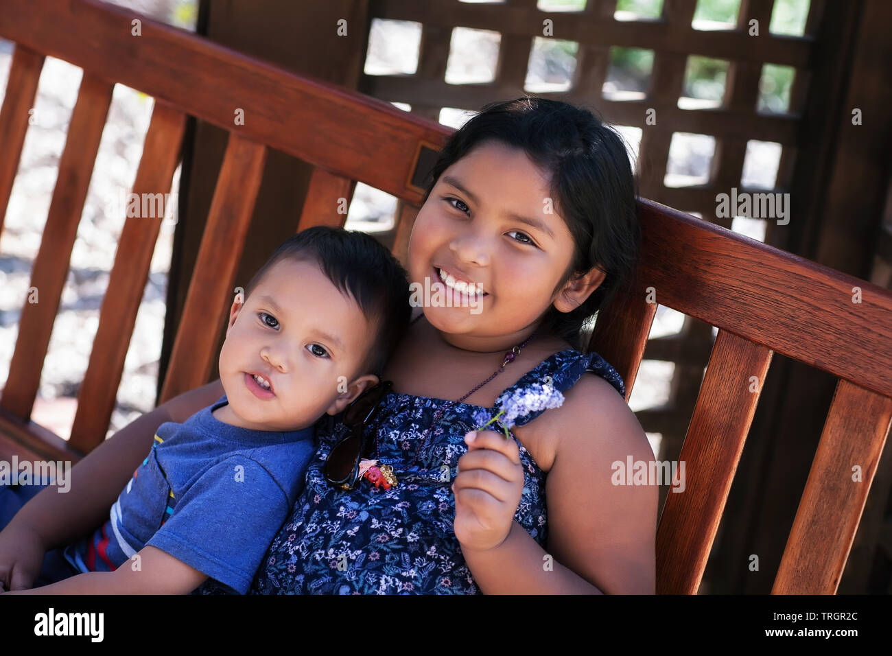 Two siblings, a young boy and older sister, sitting peacefully together on a bench. Stock Photo