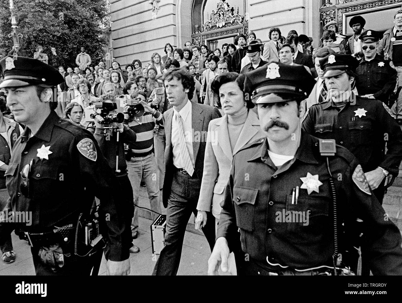 acting Mayor Dianne Feinstein and her husband Richard Blum leave San Francisco City Hall under police escort after Mayor Moscone and Harvey Milk were assassinated. San Francisco, 11/27/1978 Stock Photo