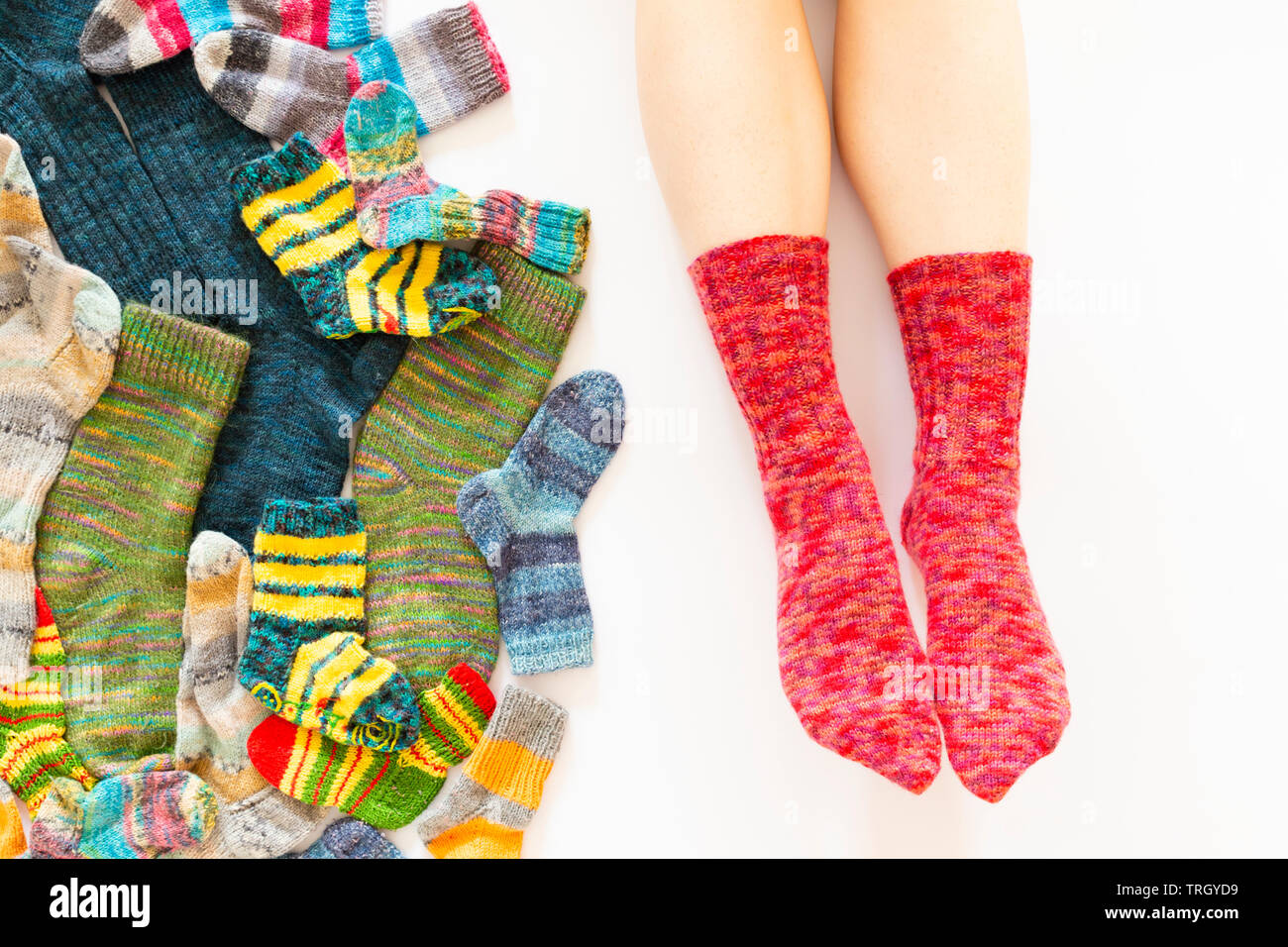 Top view of an assortment of colorful woolen socks of various sizes on white background with a pair of feet wearing red socks Stock Photo