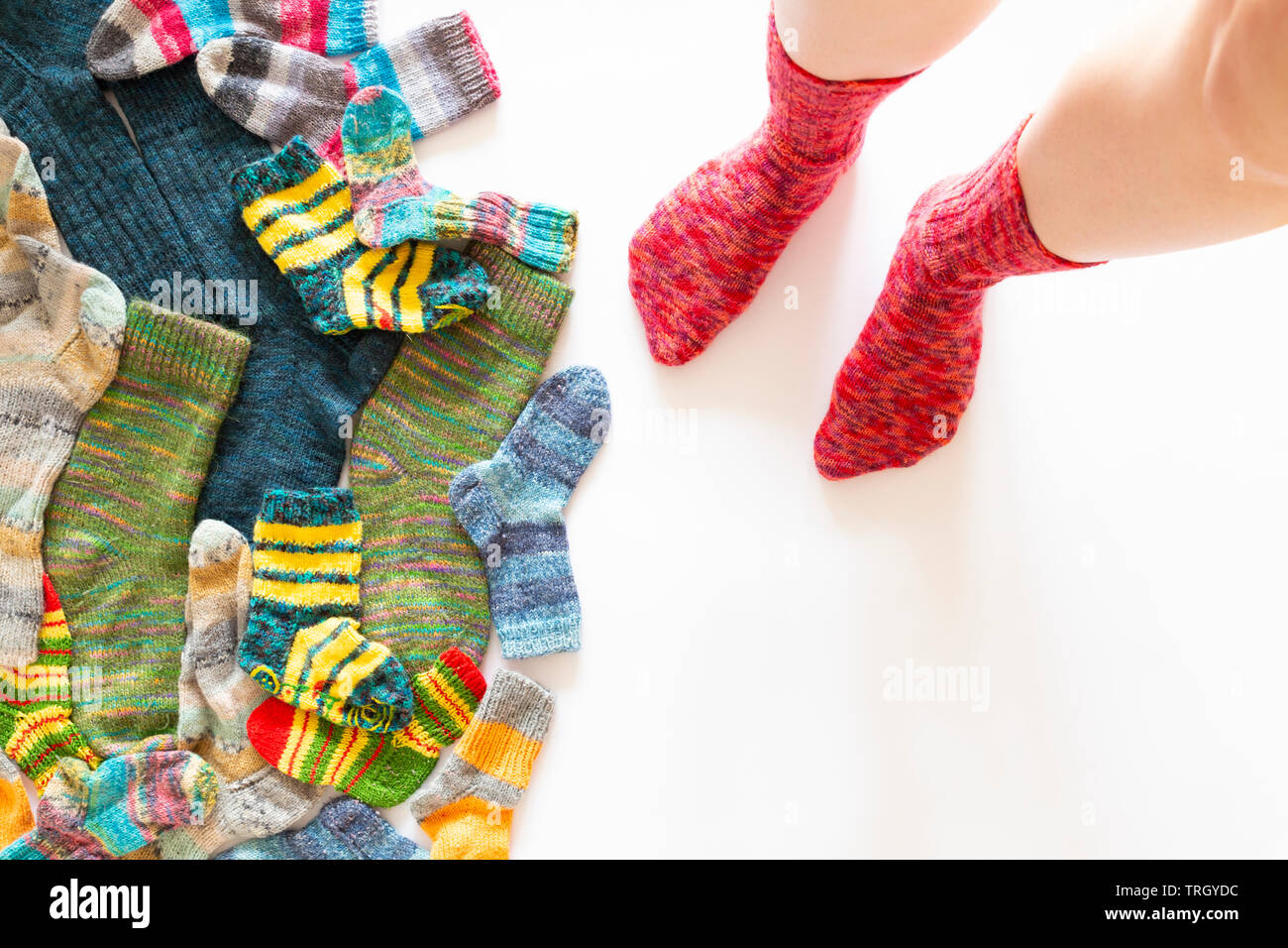 Top view of an assortment of colorful woolen socks of various sizes on white background with a pair of feet wearing red socks Stock Photo