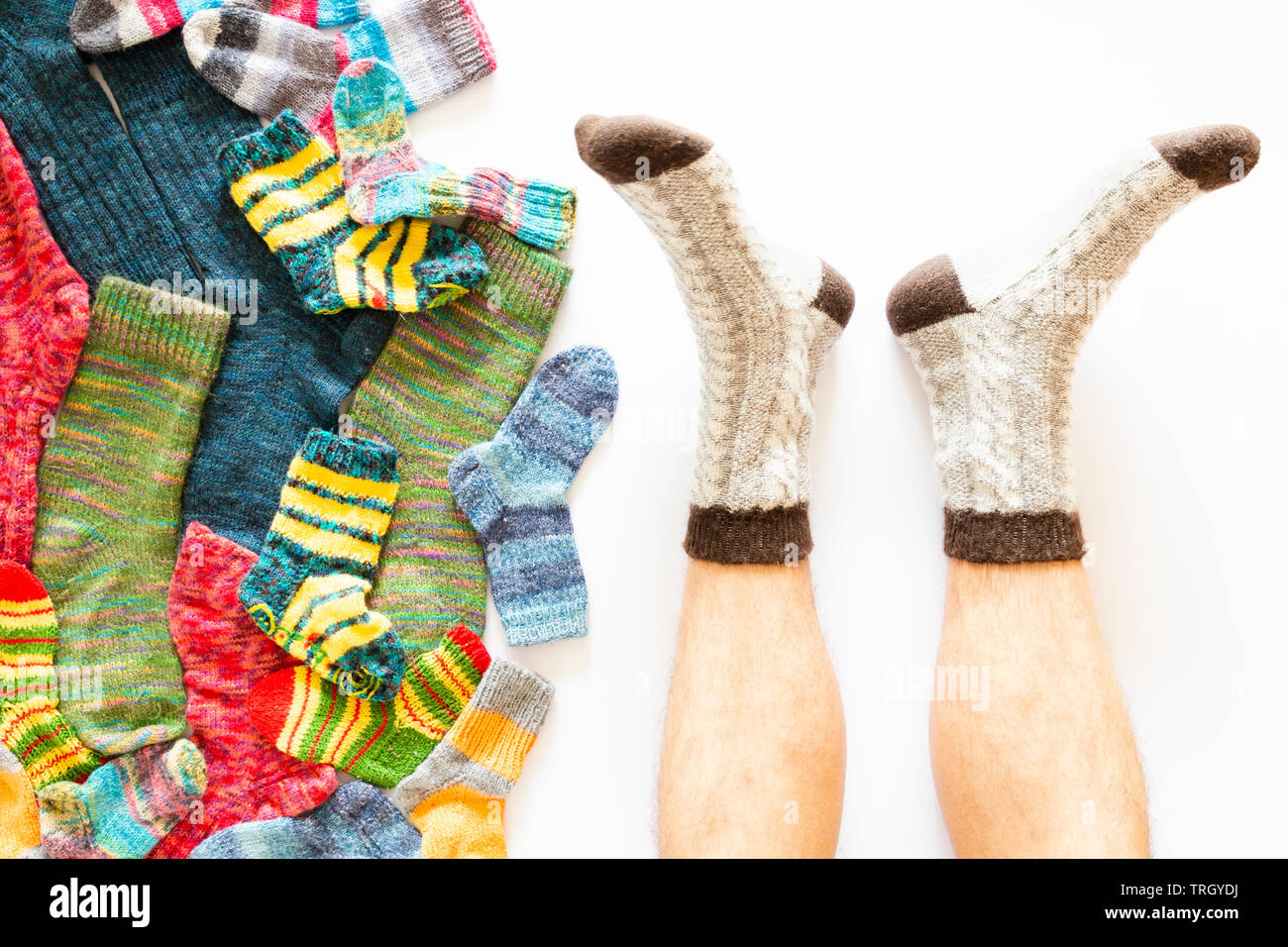 Top view of an assortment of colorful woolen socks of various sizes on white background with a pair of feet wearing gray brown socks Stock Photo