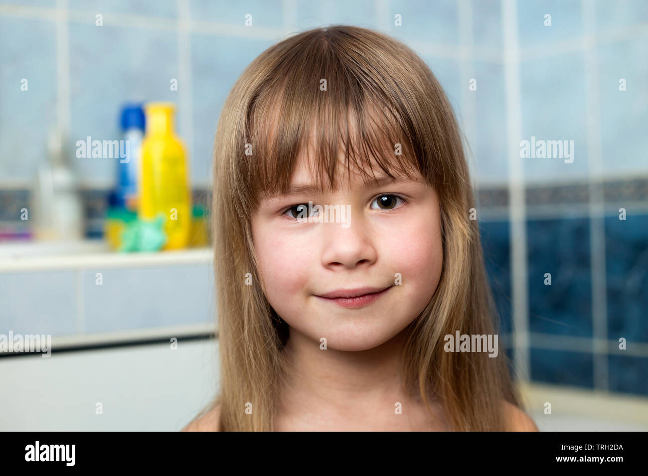 Pretty girl face portrait, smiling child with beautiful eyes and long wet fair hair on blurred background of bathroom. Stock Photo