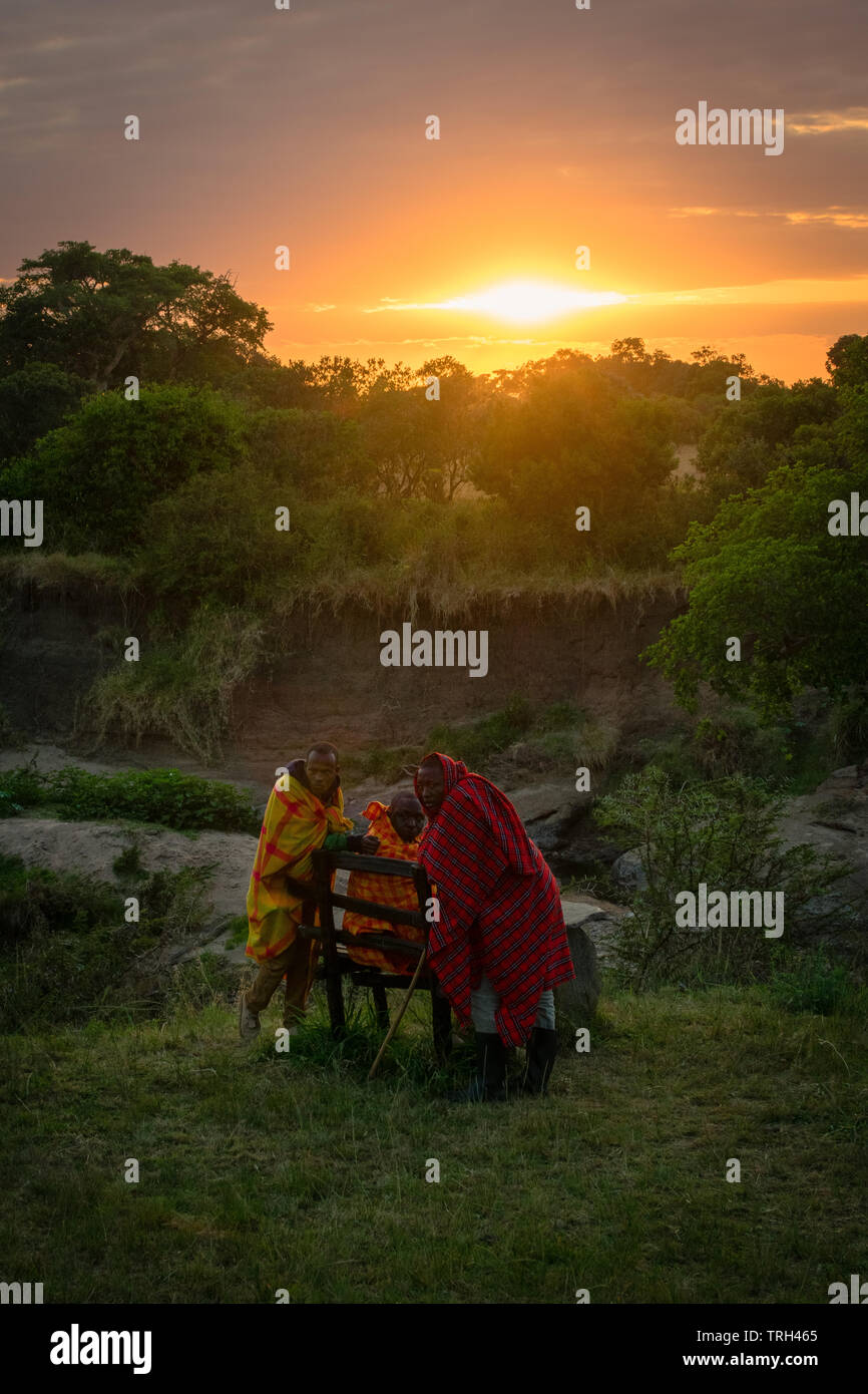 Masai Mara, Kenya, Africa – August 10, 2018: A group of Masai men in traditional clothes resting at dawn after a long night protecting tourist from da Stock Photo